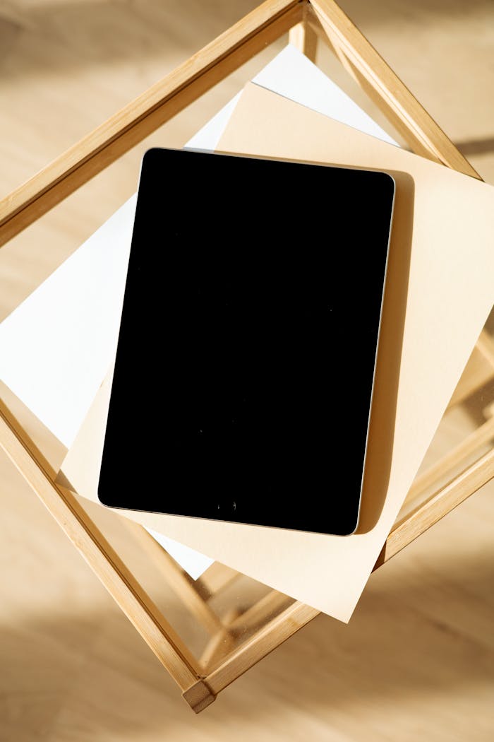Minimalist setup of a tablet on a wooden table with blank paper for mockup.